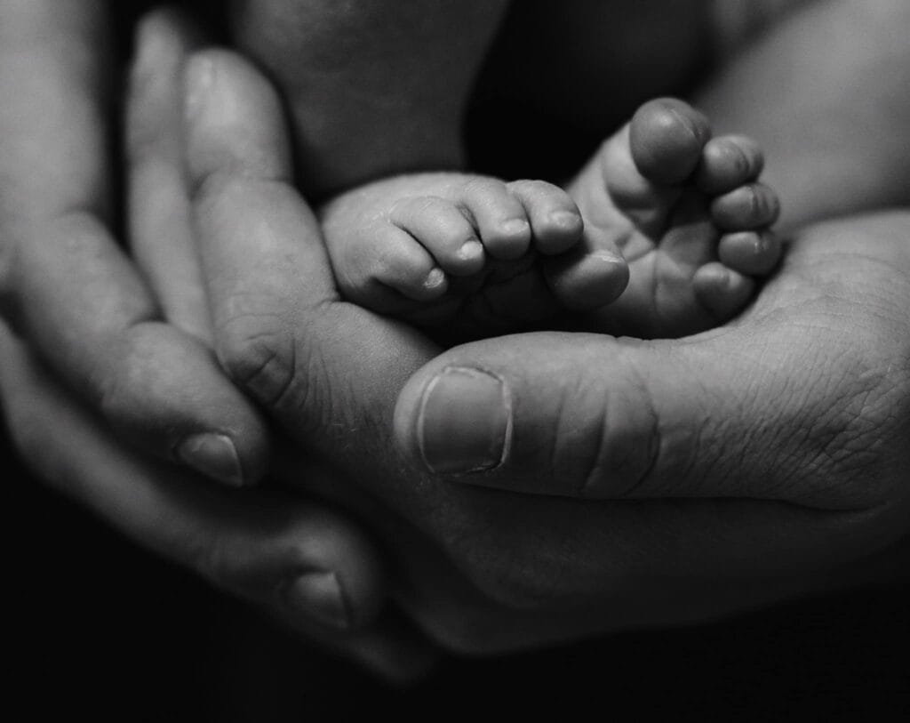 Close-up black and white image by a Yorkshire newborn baby photographer captures adult hands gently cradling a newborns tiny feet, creating a serene and tender scene.