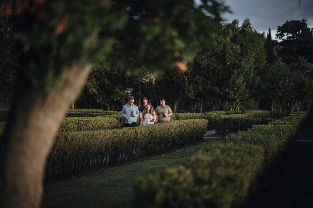 A group of five people stands in a garden maze at Villa Palazzola, surrounded by neatly trimmed hedges. Trees border the area, with oranges dotting some branches. Captured in soft, natural light, this serene scene exemplifies the charm of an Italian destination near Rome. Perfect for a wedding photographers lens.