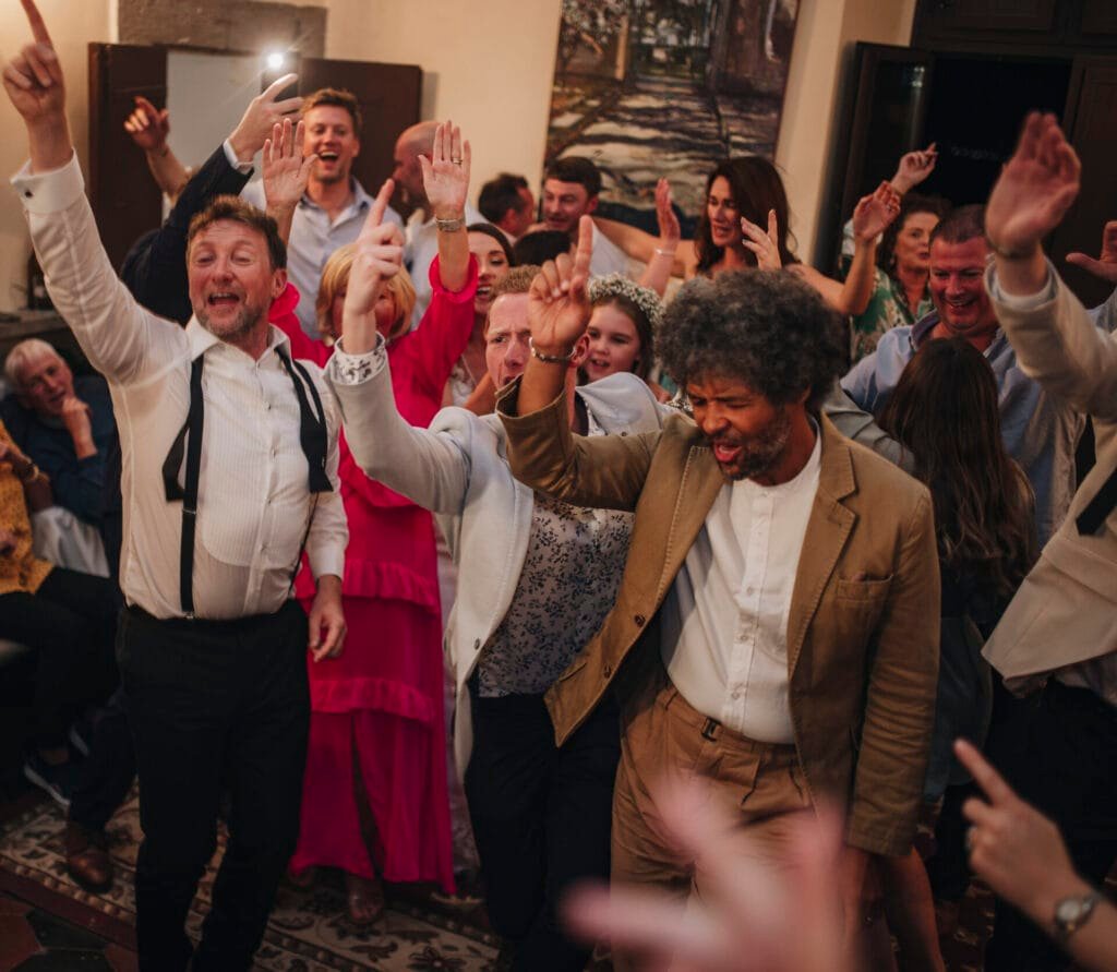 A lively group of people dancing at a Villa Palazzola wedding in Italy, some with hands raised and smiling brightly. Dressed in formal and semi-formal attire, the atmosphere is joyful and celebratory, perfect for capturing unforgettable moments as a wedding photographer in Rome.