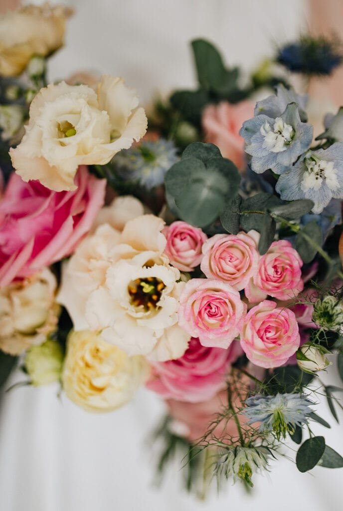 A vibrant bouquet featuring pink roses, creamy white lisianthus, soft yellow flowers, and delicate blue blooms surrounded by lush greenery—perfectly captured by a Goldsborough Hall wedding photographer.