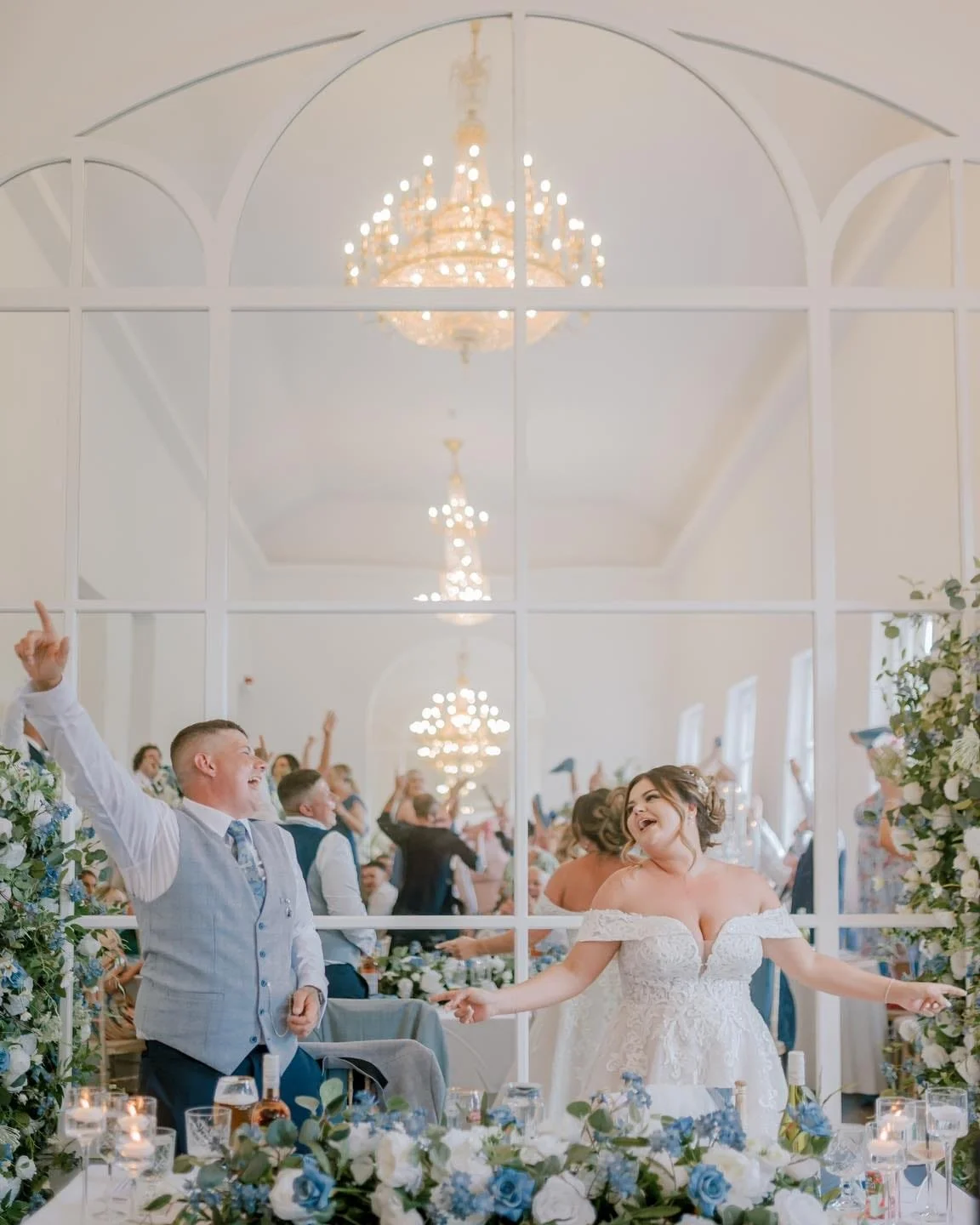 Bride and groom dancing and smiling at wedding reception with guests in the background, seen through a large decorative mirror. Take at Norwood Park during wedding breakfast