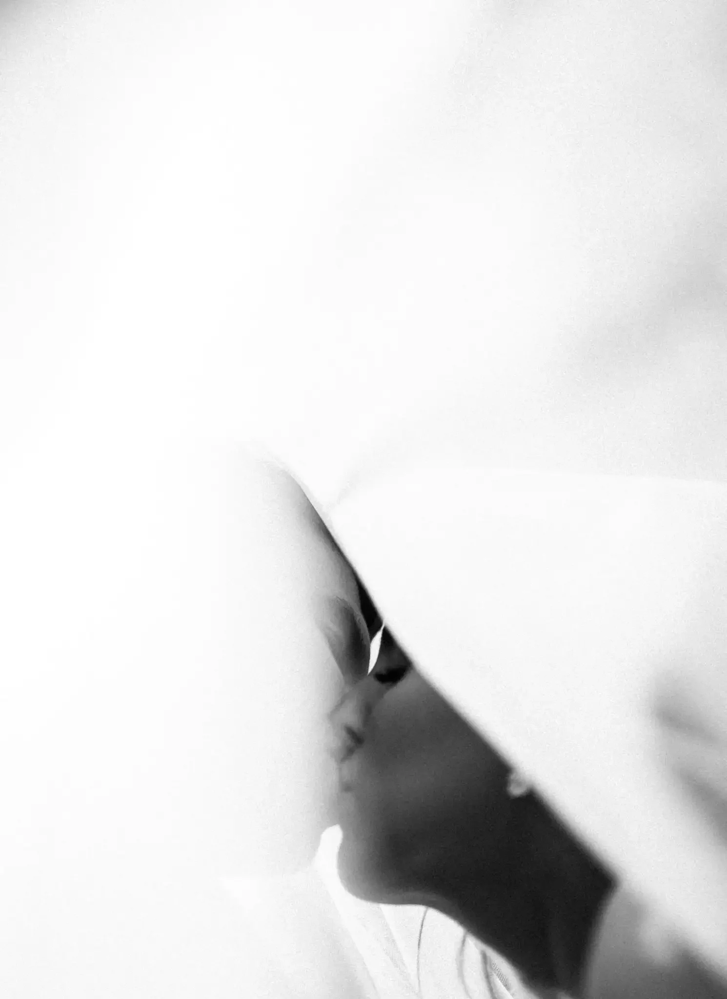 Close-up black and white photo of a woman's face partially covered by a white sheet or cloth, with focus on her lips and nose, her eyes are visible. She appears to be in a peaceful or contemplative state. taken by a norwood aprk wedding photographer