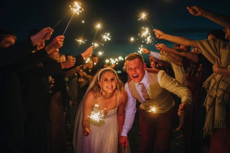 Bride and groom grinning through a sparkler send-off at Little Wold Vineyard