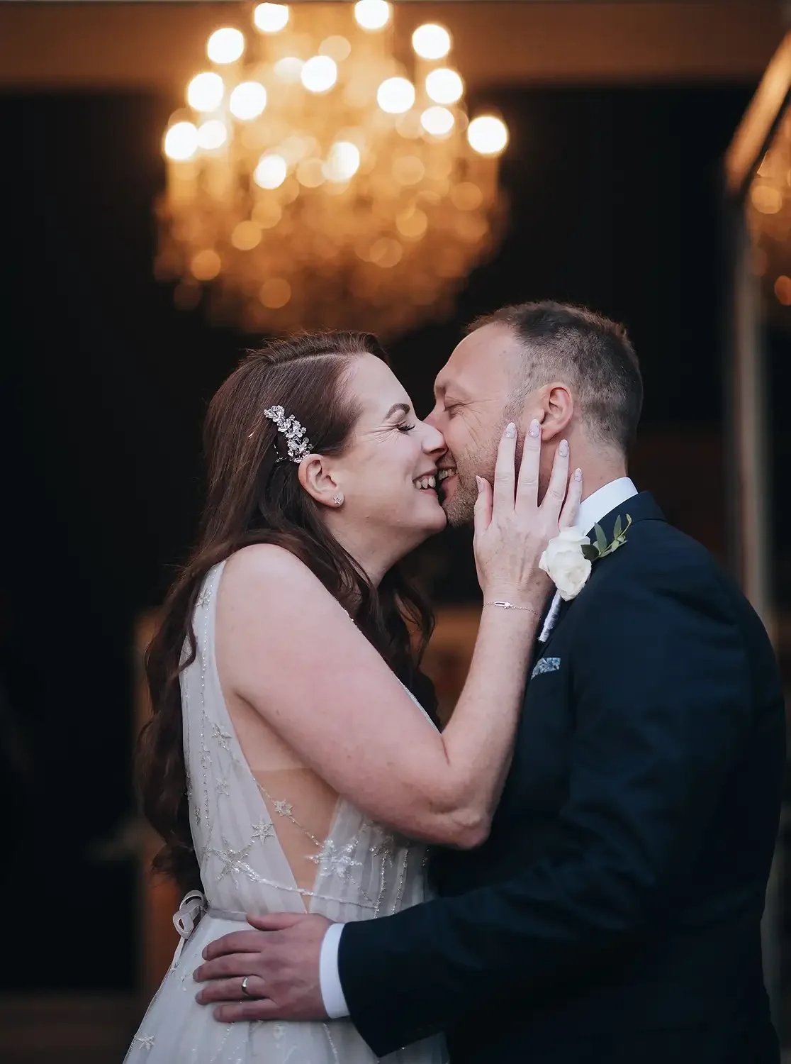 A bride and groom sharing a loving moment, touching foreheads, at their wedding reception with a chandelier in the background. Take at Hodsock Priory