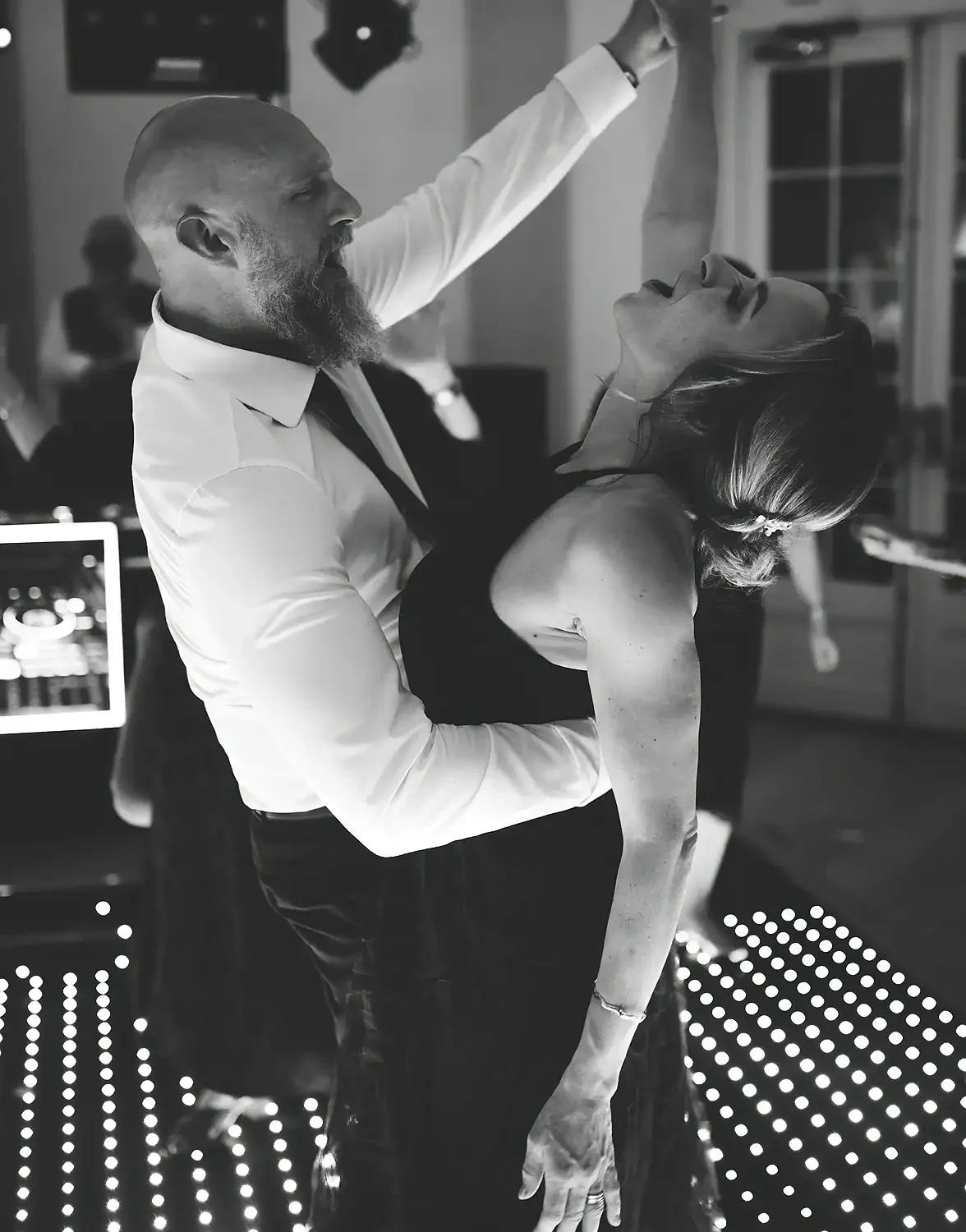 A man in a white shirt dancing with a woman in a black dress at a party, with DJ equipment visible in the background. Taken at Hodsock Priory