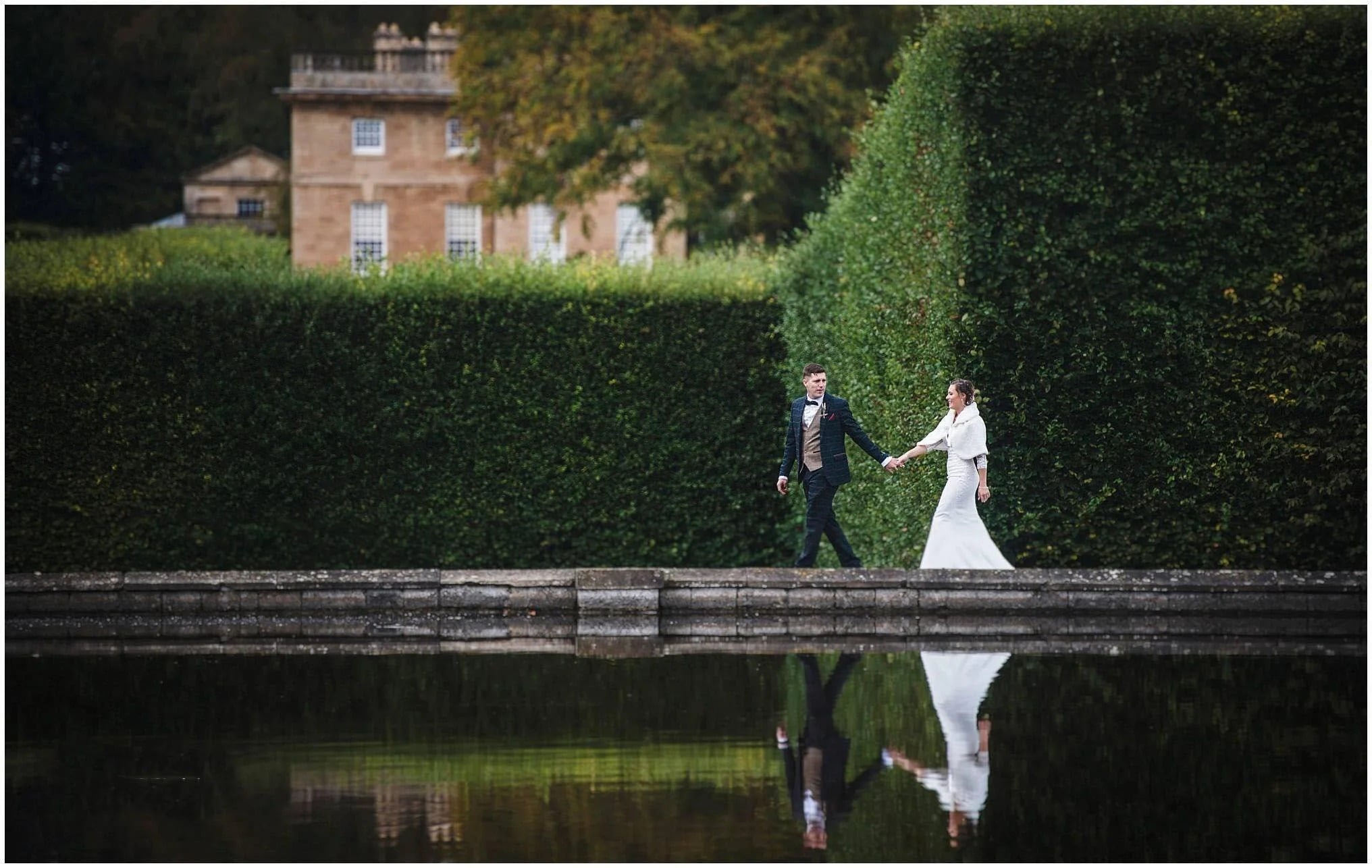 bride and groom walking hand in hand in front of lake at Bramham Park by yorkshire wedding photographer
