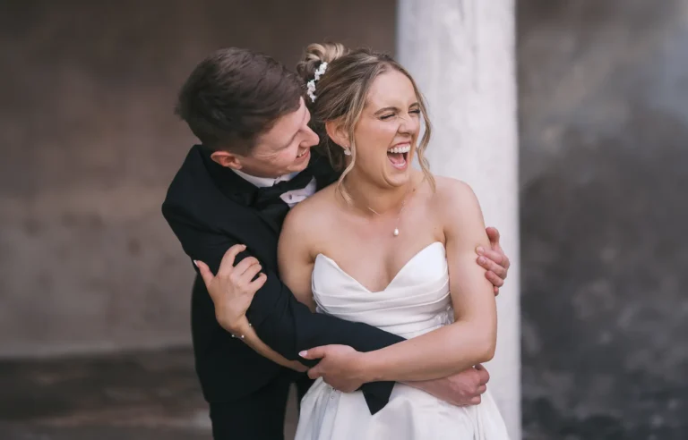 A groom playfully hugging and laughing with a bride, both dressed in wedding attire, during their wedding celebration. Taken at Norwood Park