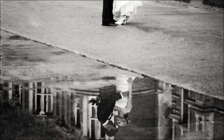 Black and white reflection in a puddle of a bride and groom kissing at Royal Holloway