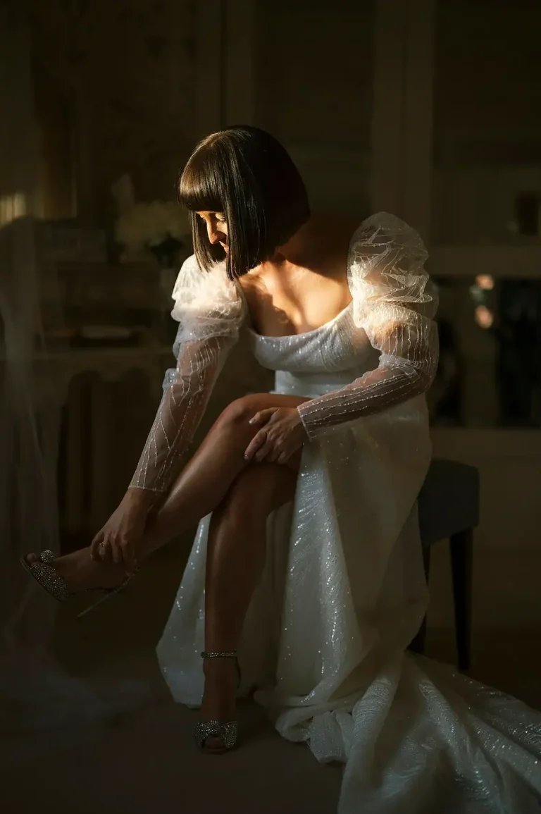 Bride adjusting her sparkly shoe in soft window light before her winter wedding at Hodsock Priory