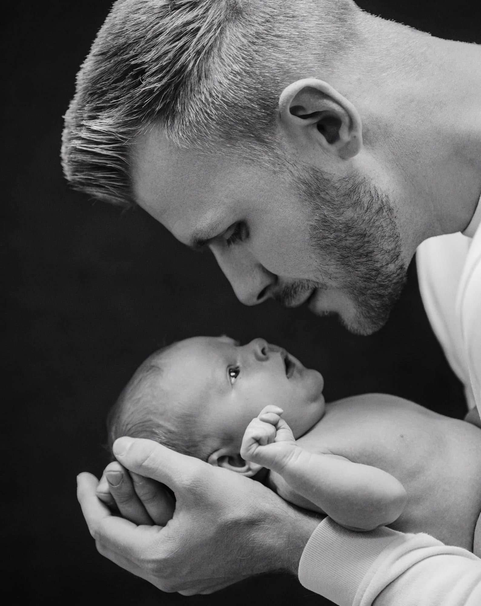 Dad looking down at his newborn son cradled in his hands, nose to nose, black and white