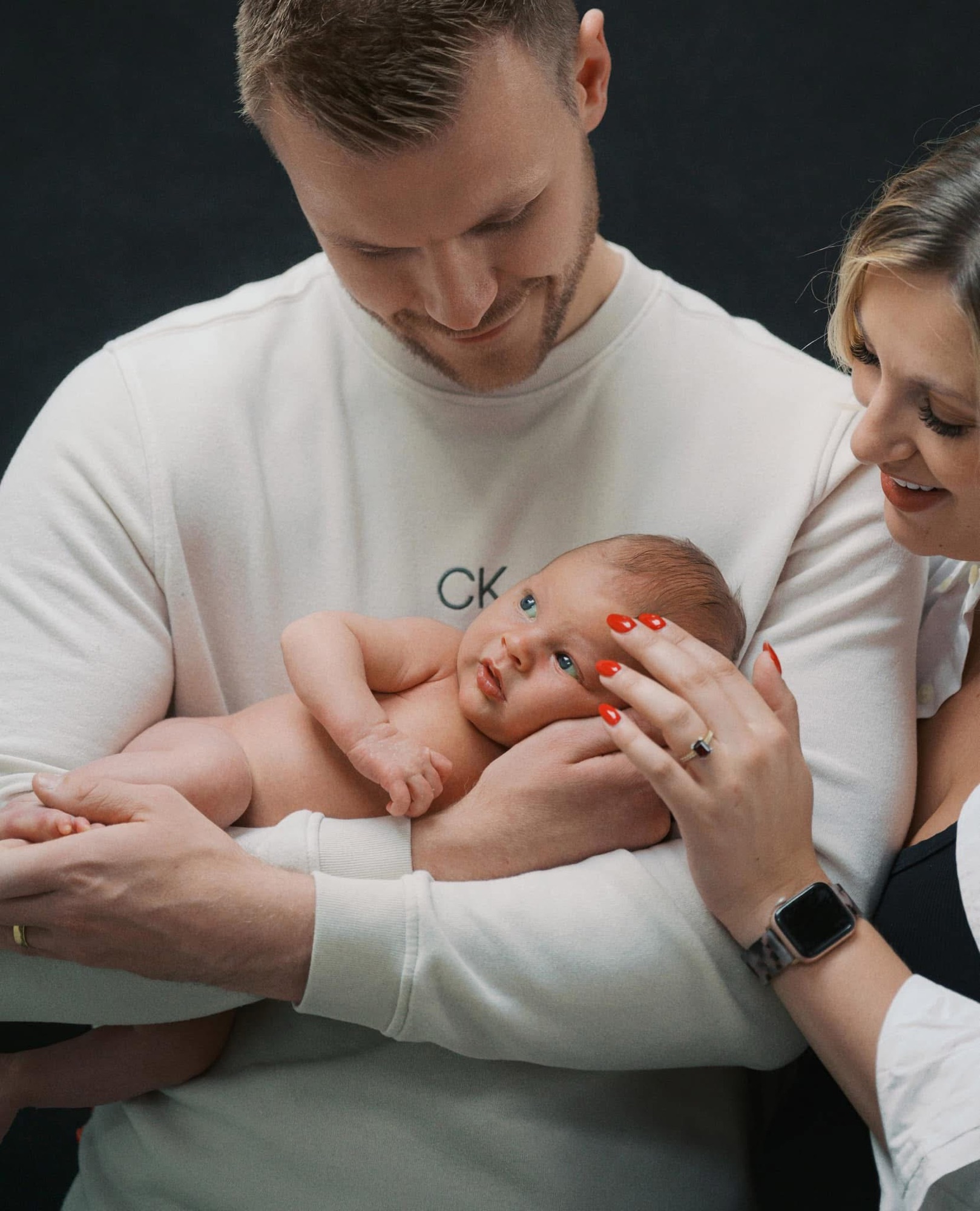 Newborn baby Archie in his dad's arms while his mum rests a hand on his head