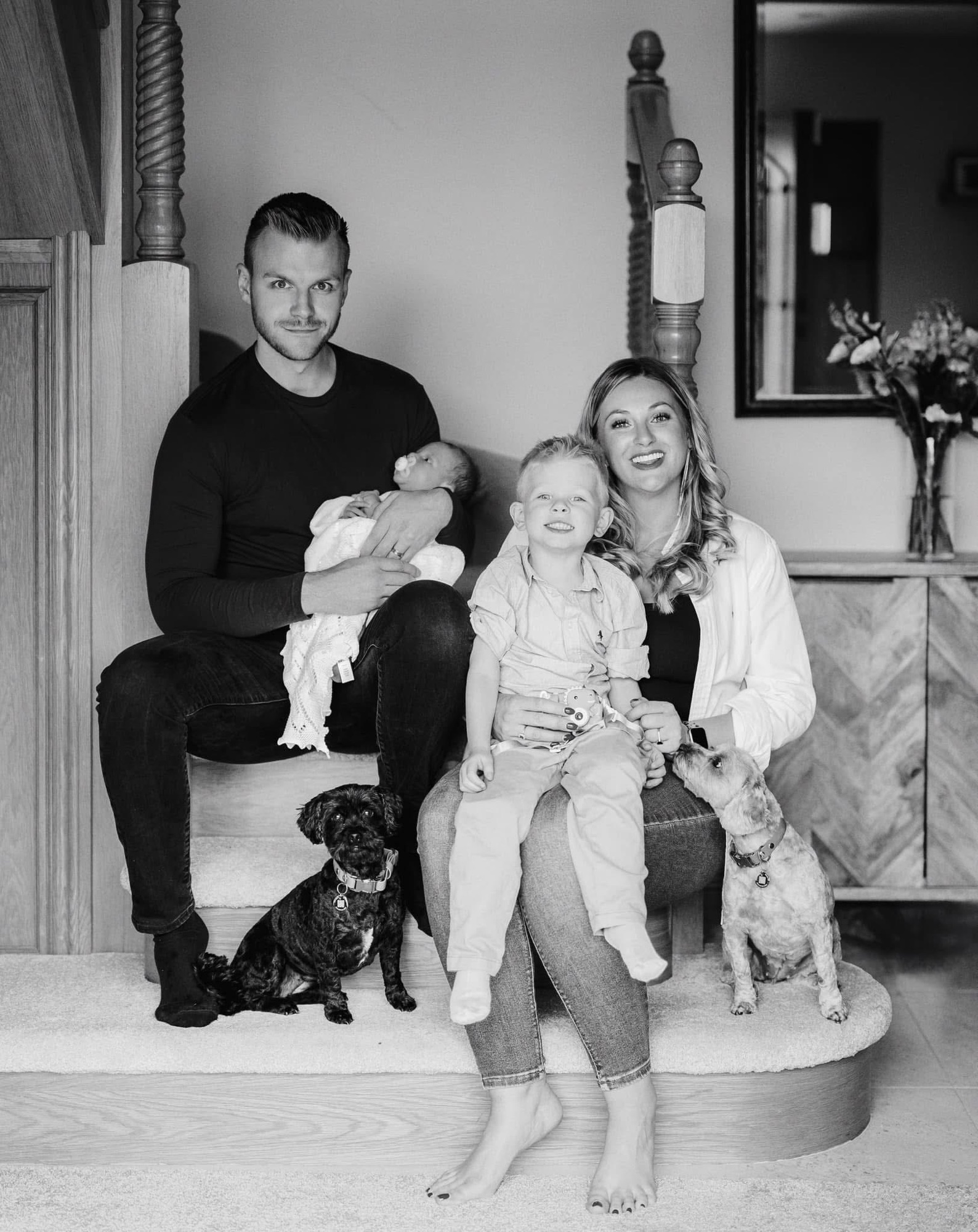 Family of four sitting on the stairs at home with their two dogs during a newborn photoshoot