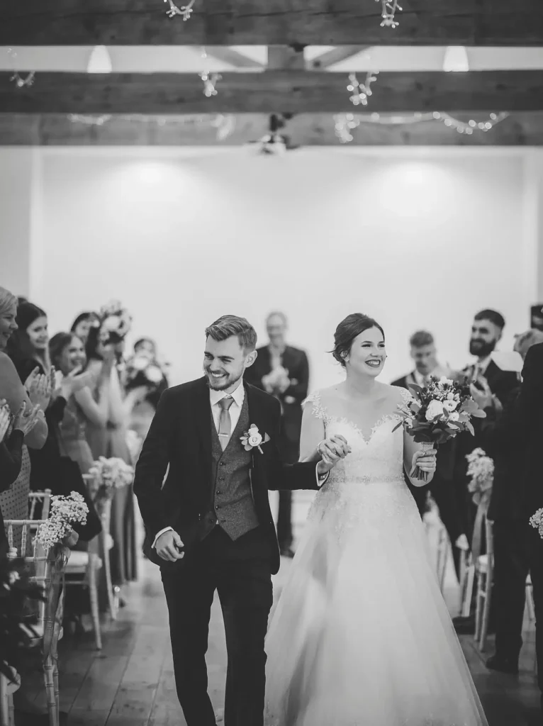 rufford mill wedding photographer brdie and groom smiling at guests as they work down the aisle together.