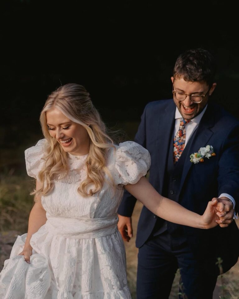 Bride and groom laughing as they walk hand in hand on a dark summer evening