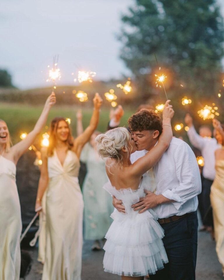 Bride and groom kissing in a sparkler send-off as the bridesmaids cheer