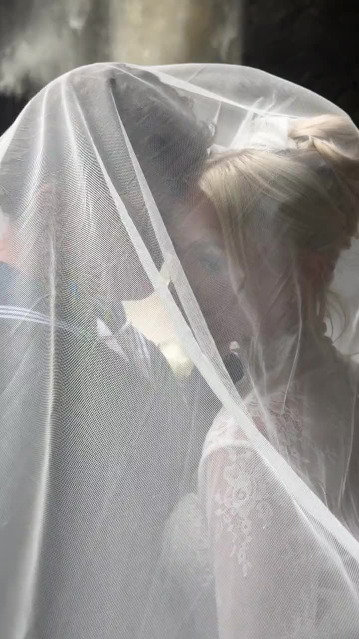 Bride and groom wrapped in her veil beside a waterfall, a short video clip